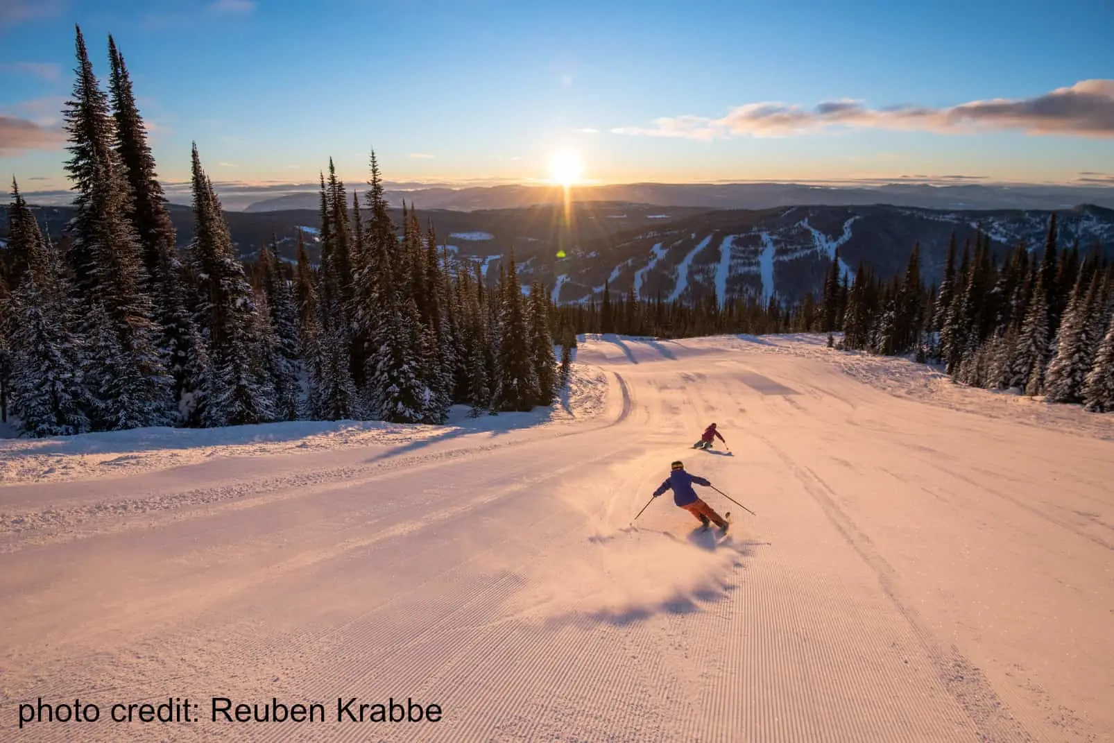 Sun Peaks 2 two skiers descending a groomed slope at sunset at Sun Peaks resort