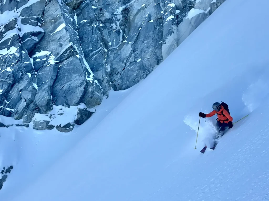 heli-skier descending a steep chute in powder
