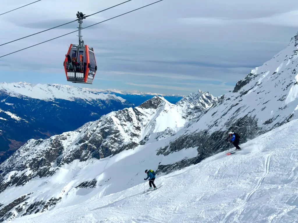 Gondola going overhead of 2 skiers in Passo Tonale