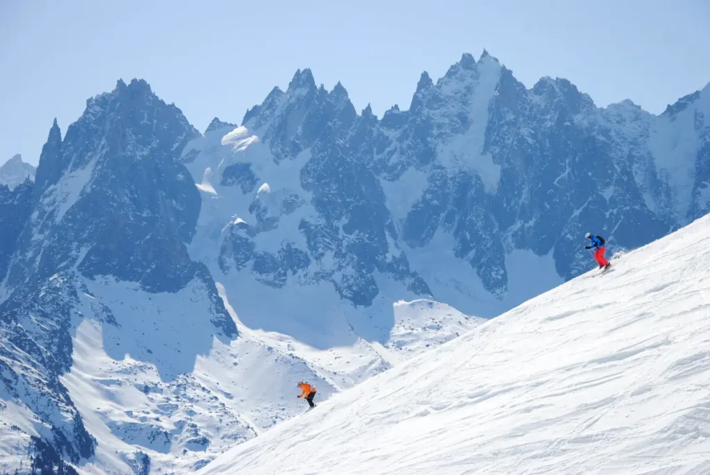 2 skiers descending Chamonix against a backdrop of jagged peaks