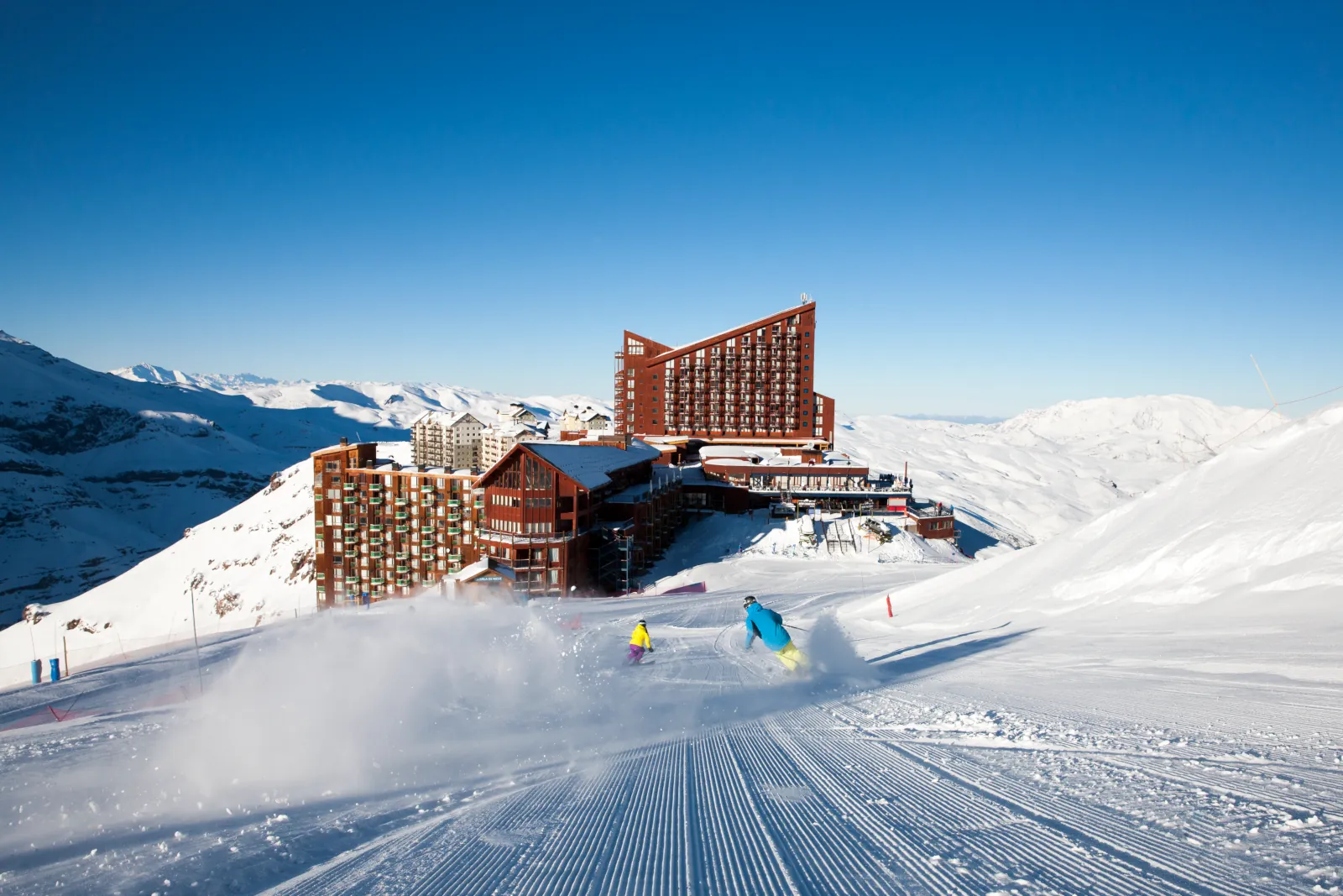 skiers descending a groomed run towards a ski resort in Chile